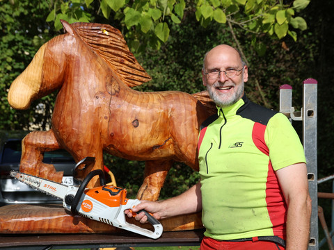 Herbstmarkt Holzkünstler mit Motorsäge neben geschnitztem Pferd beim Herbstmarkt