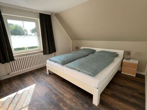 6 Schlafzimmer Schlafzimmer mit Doppelbett, blauen Decken, Dachschräge und großem Fenster.