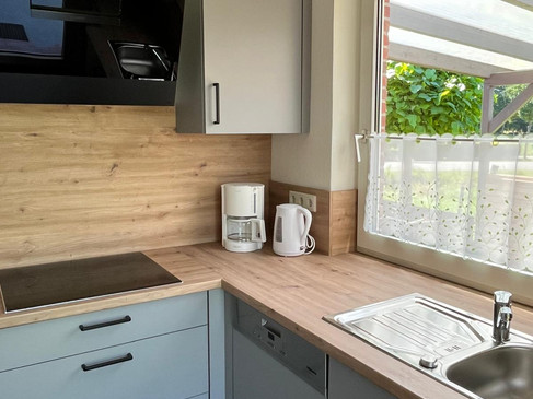 5 Küche 5.jpg Moderne Küche mit Holzarbeitsplatte, Spüle, Kochfeld, Kaffeemaschine und Fenster.