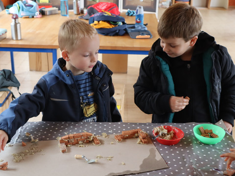 Herbstferienprogramm auf :metabolon Zwei Kinder bauen an einem Tisch mit Mini-Ziegeln und Lehm kleine Mauern.