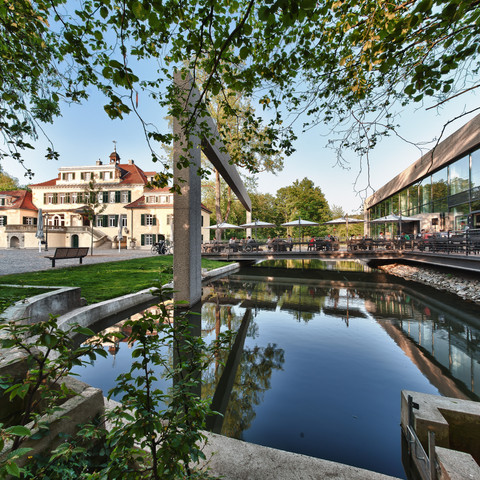Haus Eulenbroich Historisches Herrenhaus mit rotem Dach, umgeben von Bäumen, neben einem modernem Gebäude und Teich.