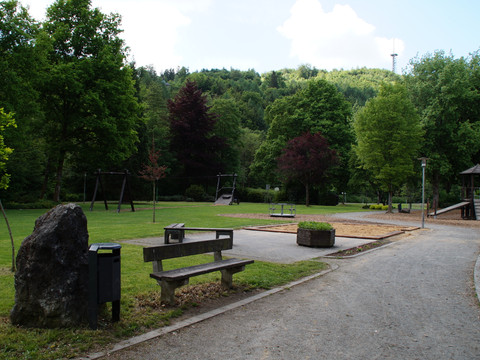 Kurpark mit Spielplatz <p>Ein grüner Park mit Bänken, Spielplatz, Bäumen und einem Kiesweg in einer ländlichen Umgebung.</p>