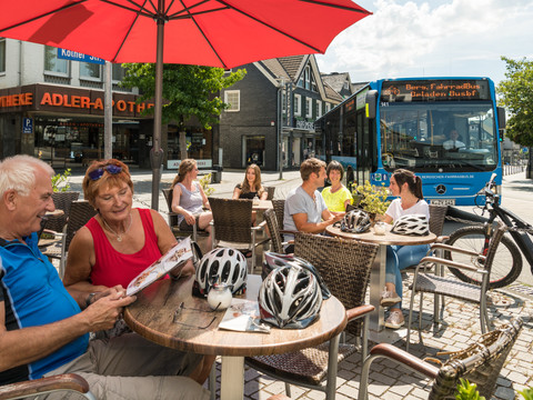 Eiscafé im Ortskern <p>Menschen sitzen unter Sonnenschirmen vor einem Café, während ein Linienbus im Hintergrund hält.</p>