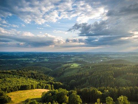 Reichshof Blockhaus Weitläufige, grüne Landschaft mit Wäldern und Hügeln unter einem bewölkten, doch lichtdurchfluteten Himmel.