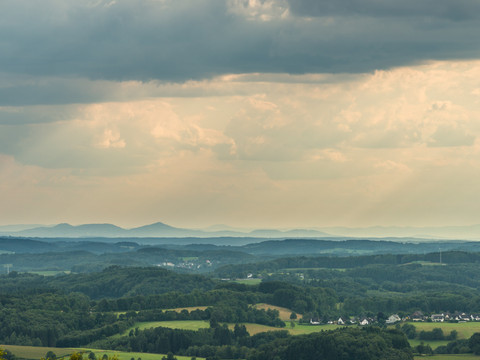 Blick in Richtung Siebengebirge von Blockhaus Weitläufige Hügellandschaft im Reichshof mit bewaldeten Flächen und Dörfern unter bewölktem Himmel.