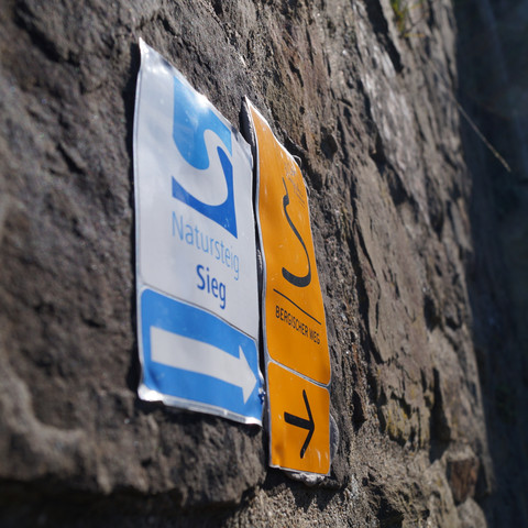 Markierung an der Stadtmauer <p>Wegweiser am Natursteig Sieg auf einer steinernen Wand, zeigen Richtung "Natursteig Sieg".</p>