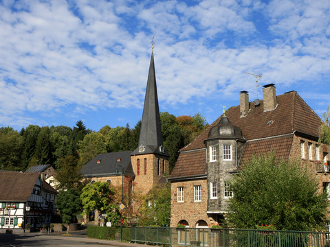 Ortsansicht  Eine idyllische Dorfkirche und Fachwerkhäuser unter blauem Himmel mit weißen Wolken.