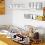 pension-zurweser-fruehstueck Frühstücksbuffet mit Cerealien, Marmelade und Saft, vor warmen Erdfarben und schlichtem Geschirr.