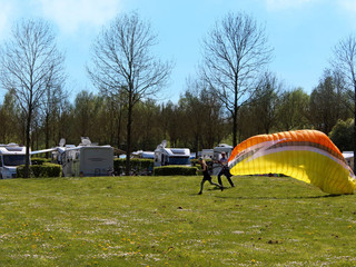 wohnmobil-freizeitanlage-godelheim-paraglider Paragleiter startet auf einer grünen Wiese, im Hintergrund stehen Wohnmobile unter Bäumen.