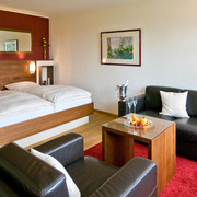 hotel_rosenberg_bad-driburg_1600 Modernes Hotelzimmer mit Doppelbett, Ledersofas, Couchtisch, Sektkühler, hellem Holzboden und Wandkunst.