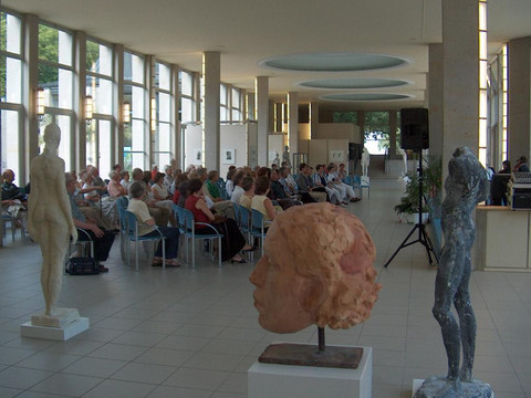 Innenraum einer Kunsthalle mit großen Fenstern, besetzt von Personen, Skulpturen im Vordergrund.Interior of an art gallery with large windows, occupied by people, sculptures in the foreground.Interiér umělecké galerie s velkými okny, obsazený lidmi, v popředí sochy.Wnętrze galerii sztuki z dużymi oknami, zajęte przez ludzi, rzeźby na pierwszym planie.Interieur van een kunstgalerie met grote ramen, bezet door mensen, beelden op de voorgrond.Interno di una galleria d'arte con grandi finestre, occupata da persone, sculture in primo piano.