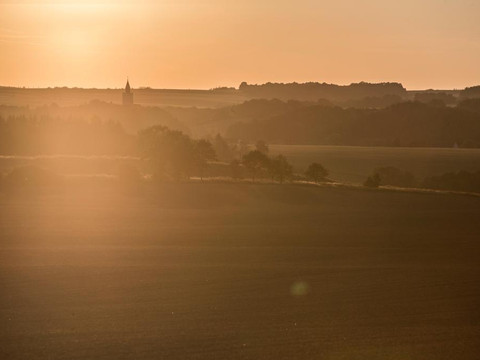 Morgennebel über sanften Hügeln, im Hintergrund ein Kirchturm bei Sonnenaufgang.Morning mist over rolling hills, a church tower in the background at sunrise.Ranní mlha nad kopci, v pozadí kostelní věž při východu slunce.Poranna mgła nad wzgórzami, wieża kościoła w tle o wschodzie słońca.Ochtendnevel over glooiende heuvels, een kerktoren op de achtergrond bij zonsopgang.Nebbia mattutina su dolci colline, sullo sfondo il campanile di una chiesa al sorgere del sole.