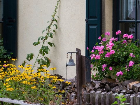 Blumenreicher Bauerngarten mit gelben und rosa Blüten, historische Gebäude im Hintergrund.Flower-filled cottage garden with yellow and pink blossoms, historic buildings in the background.Květinová zahrada u chalupy se žlutými a růžovými květy, v pozadí historické budovy.Ukwiecony przydomowy ogród z żółtymi i różowymi kwiatami, zabytkowe budynki w tle.Bloemrijke cottage tuin met gele en roze bloesems, historische gebouwen op de achtergrond.Giardino fiorito con fiori gialli e rosa, edifici storici sullo sfondo.