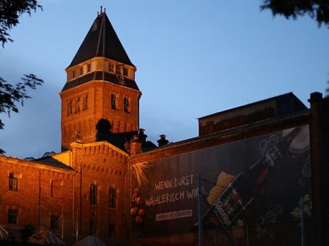 Köstritzer Brauerei Gutshof in de schemering met verlichte bakstenen toren en reclamebanner.