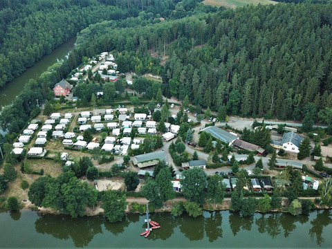 Naturcampingplatz Weida Luftaufnahme eines Naturcampingplatzes am Waldrand mit vielen Wohnwagen entlang eines Flusses.