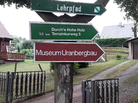 Wegweiser aus Holz mit Richtungsschildern zu einem Lehrpfad und dem Museum Uranbergbau.Wooden signpost with directional signs to a nature trail and the uranium mining museum.Dřevěný rozcestník se směrovkami k naučné stezce a muzeu uranového hornictví.Drewniany drogowskaz z kierunkowskazami do ścieżki przyrodniczej i muzeum górnictwa uranu.Houten wegwijzer met richtingaanwijzers naar een natuurpad en het uraniummijnmuseum.Cartello in legno con indicazioni per il sentiero naturalistico e il museo dell'estrazione dell'uranio.