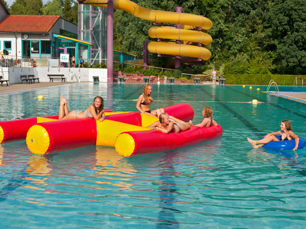Hallen- und Freibad Wingst Jugendliche entspannen auf bunten Wasserattraktionen im Freibad Wingst vor großer gelber Rutsche.