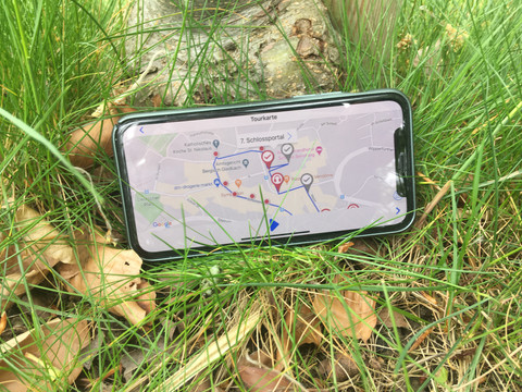 Lauschtour Bensberg auf der Karte in der App Smartphone mit geöffneter Karten-App liegt im Grünen auf Gras neben Laub und einem Baumstamm.