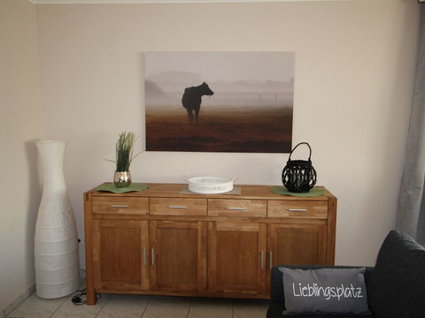 Wohnzimmer Wohnzimmer mit Holzmöbeln und Naturdeko, Kuhbild an der Wand, "Lieblingsplatz"-Kissen auf Sofa.