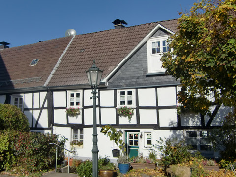 In der Altstadt Bergneustadt Fachwerkhaus mit weißer Fassade und schwarzen Balken, umgeben von Herbstbäumen und Laterne.