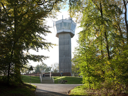 Wingst Aussichtsturm Deutscher Olymp Aussichtsturm Deutscher Olymp im Wald, von Sonnenlicht umgeben, mit Weg und Fahrrädern davor.