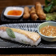 Restaurant Lua by Danny Nahaufnahme einer Sommerrolle mit einem Schälchen Erdnusssoße. Close-up of a summer roll with a small bowl of peanut sauce.