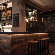 Bar em Schnörres Holzverkleidete Bartheke mit Hockern in schummrigem Licht. Eine Kreidetafel ziert die komplette hintere Wand mit Kritzeleien drauf.Wood-paneled bar with stools in dim light. A chalkboard adorns the entire back wall with scribbles on it.