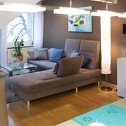 fewo-startpunkt1-wohnzimmer1.jpg Gemütliches Wohnzimmer mit grauem Sofa, Glastisch, modernen Kunstwerken und elegantem Dekor.