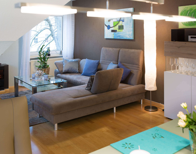 fewo-startpunkt1-wohnzimmer1.jpg Gemütliches Wohnzimmer mit grauem Sofa, Glastisch, modernen Kunstwerken und elegantem Dekor.