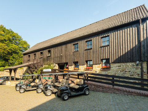 Golfclub Burg Overbach Golfcarts stehen vor einer rustikalen Holzhütte mit blühenden Blumen auf einem Pflastersteinplatz.