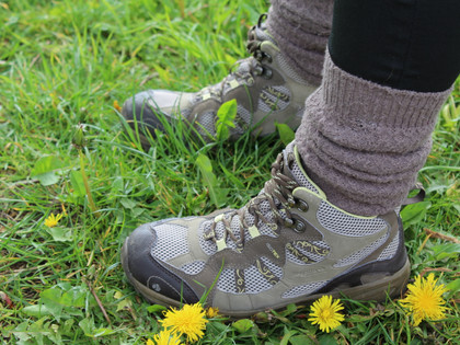 Wandern Robuste Wanderstiefel stehen in lebendig grünem Gras, umgeben von blühendem Löwenzahn.