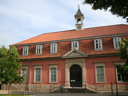 Romantik Bad Rehburg Längliches Gebäude mit rotem Ziegeldach, Uhrturm, symmetrischen Fenstern und einem steinernen Eingang.