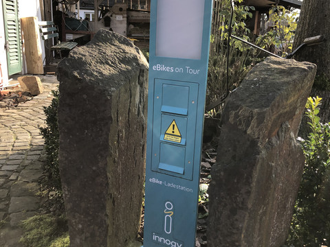 Ladesäule für E-Bikes Die Ladestation für E-Bikes steht zwischen zwei Steinen in einer sonnigen Hofeinfahrt.