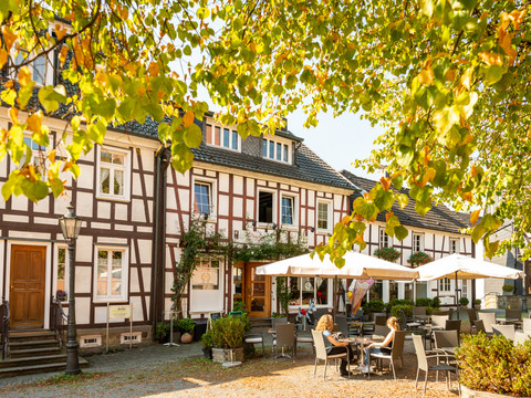 Innenstadt Fachwerkgebäude mit Herbstlaub, Sonnenschirmen und Gästen im Außenbereich. Warme, einladende Atmosphäre.