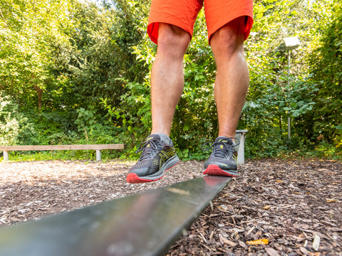 Kneipp-Vitalpark Balancierende Füße in Sportschuhen auf einem Balken im Wald, mit grünen Bäumen im Hintergrund.