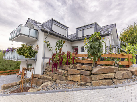 Camping "Am Mühlenberg" Zweistöckiges, modernes Haus mit grauem Dach, umgeben von gepflegtem Garten und Pflanzungen.