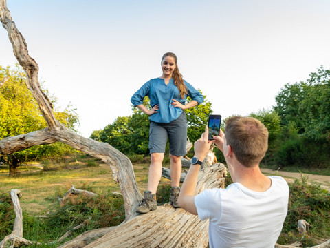 Wahner Heide <p>Frau posiert auf einem umgestürzten Baum, während Mann Foto in sonniger Natur macht.</p>