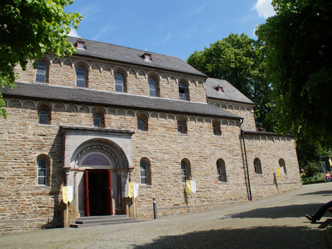 Basilika St. Gertrud Die Abtei Rolduc im Grünen mit romanischer Architektur und bunten Fahnen vor dem Eingang.