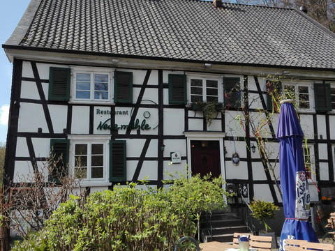 Restaurant Neuemühle Fachwerkhaus mit grünen Fensterläden, Restaurant Neumühle, Terrasse mit Sonnenschirm und Tischen.