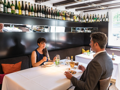 Hotel Zur Post Ein elegantes Restaurant mit zwei Personen, die an einem weißen Tisch essen. Weinflaschen zieren die Wand.