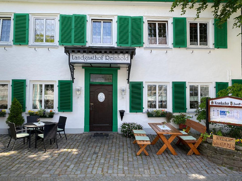 Draußen_1.jpg Fassade eines traditionellen Gasthauses mit grünen Fensterläden, Holzbänken und Pflanzendekoration.