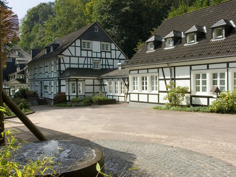 Seminar- und Tagungshotel Große Ledder Fachwerkhäuser umgeben von grünen Bäumen unter blauem Himmel; teilweise gepflasterter Vorgarten.