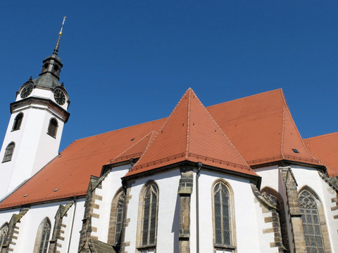 Torgau-Marienkirche_WG_DSCF6629.jpg Weiße Kirche mit roten Ziegeldächern und gotischen Fenstern unter strahlend blauem Himmel.