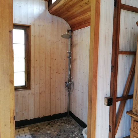 Badezimmer Gemütliches Badezimmer aus Holz mit Schrägdach, Dusche und Fenster, das Tageslicht hereinlässt.