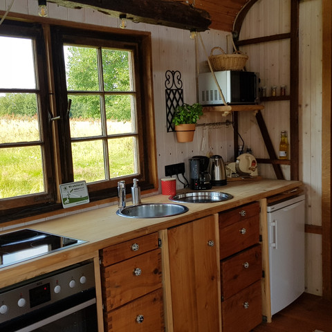 Küche Gemütliche Küchenzeile aus Holz mit Herd, Spüle und Fenster, das auf eine grüne Wiese blickt.