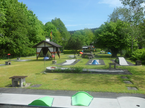 Minigolfplatz in Reichshof-Eckenhagen Minigolfplatz mit gepflegten Grünflächen, bunten Hindernissen, umgeben von Bäumen an einem sonnigen Tag.