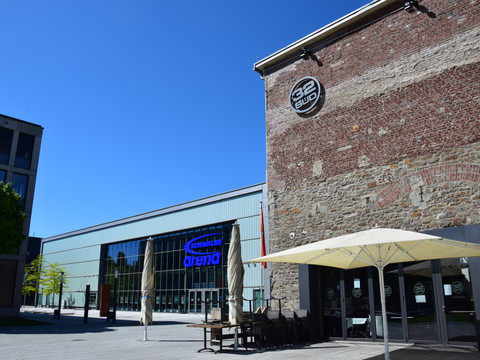 Steinmüllergelände Veranstaltungshalle "Halle 32" (Schwalbe Arena) Gummersbach: Historische Fassade neben moderner Schwalbe-Arena bei strahlend blauem Himmel.
