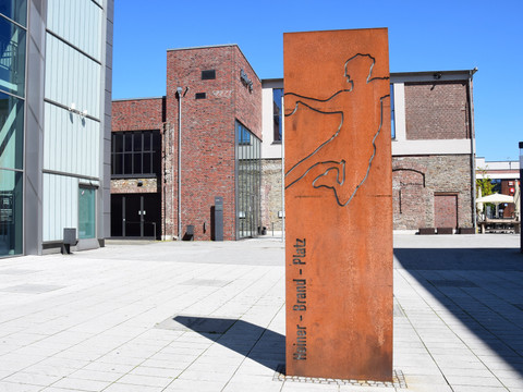 Steinmüllergelände <p>Rostfarbene Skulptur eines springenden Mannes vor modernen und historischen Gebäuden in Gummersbach.</p>