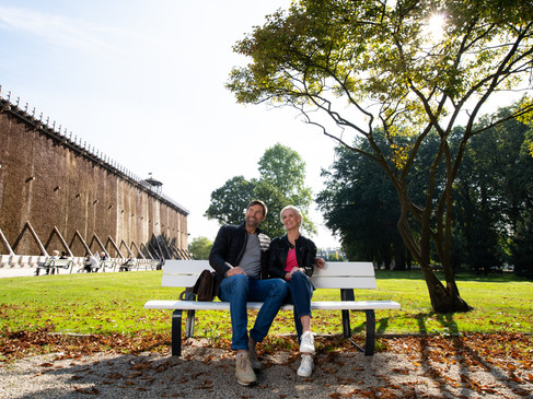 Ein Paar sitzt entspannt auf einer Parkbank vor einer Gradierwand an einem sonnigen Tag.A couple sits relaxing on a park bench in front of a graduation wall on a sunny day.Et par sidder og slapper af på en parkbænk foran en gradueringsvæg på en solskinsdag.Een stel zit ontspannen op een bankje in het park voor een afstudeermuur op een zonnige dag.