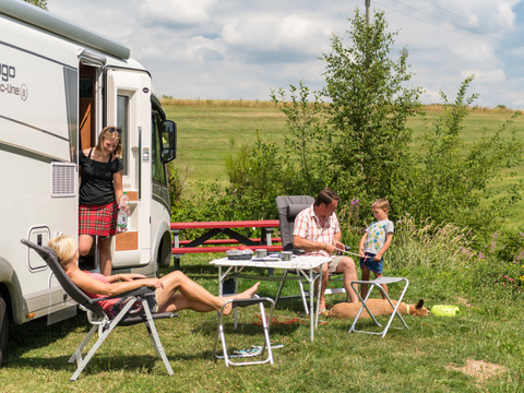 Campingpark im Bergischen Land Familie genießt Camping neben Wohnmobil auf grüner Wiese mit Picknicktisch unter freiem Himmel.